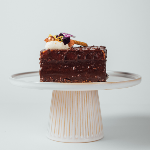 Chocolate cake slice on a white pedestal stand.