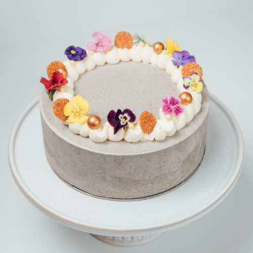 A decorated cake with colorful flowers and sprinkles on a white stand.