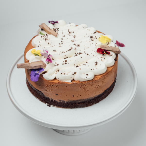 Chocolate cake with whipped cream and edible flowers on a white stand.