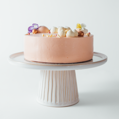 Peach-colored cake with flowers and meringue on a white stand.