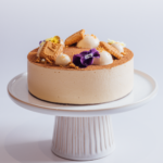 Creamy cake with cookies and edible flowers on a white stand.