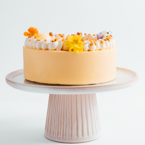 Orange cake with white frosting and flowers on a pedestal stand.