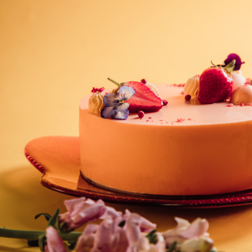 Orange cake with strawberries and flowers on a red plate.