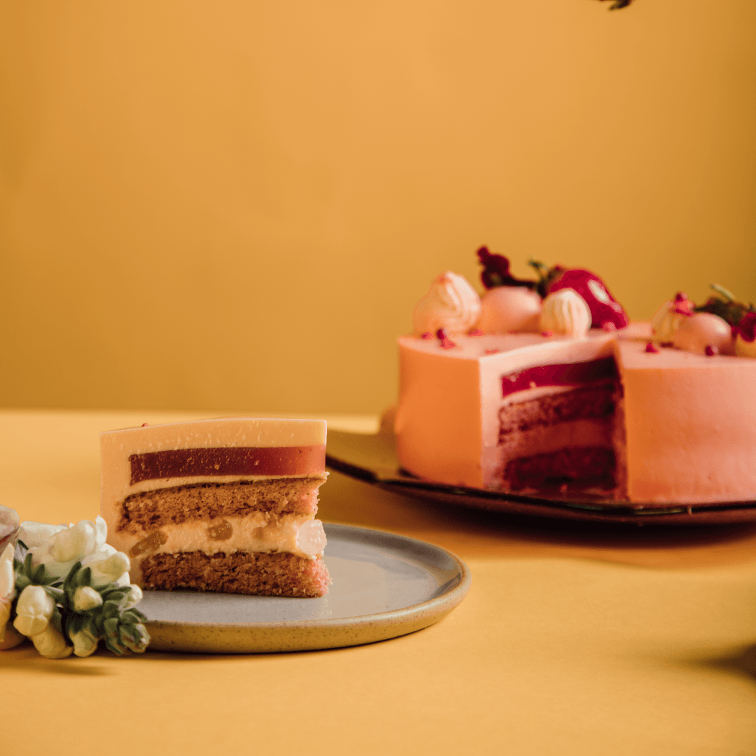 Slice of layered cake on plate, whole cake in background, yellow backdrop.