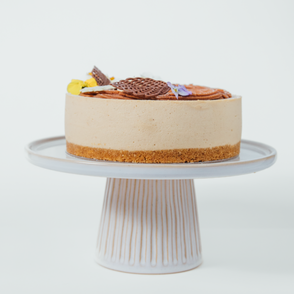 A cheesecake on a white cake stand with chocolate decorations.