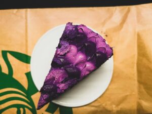 Slice of purple cake on a white plate with a brown background.