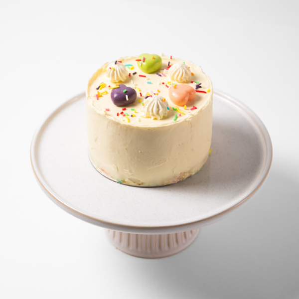 A decorated cake with colorful toppings on a white stand.