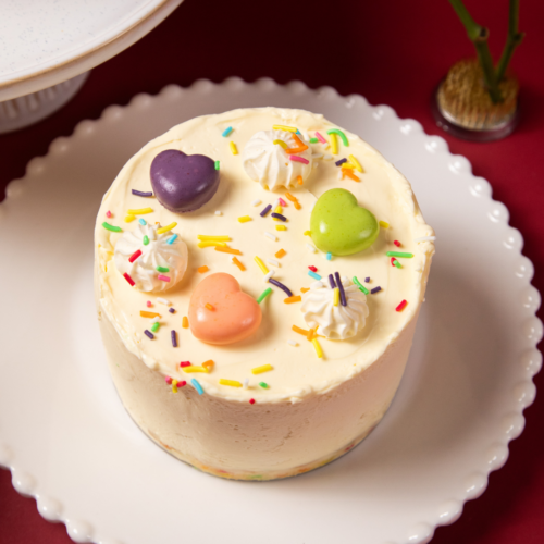 Colorful heart-decorated cake with sprinkles on a white plate.