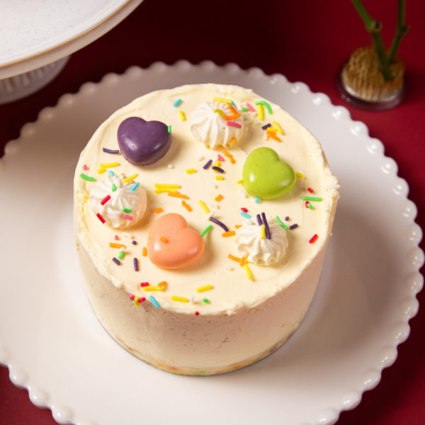Colorful heart-decorated cake with sprinkles on a white plate.