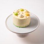 Small frosted cake with colorful decorations on a white stand.