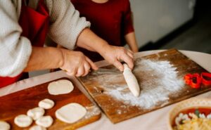Person rolling dough on a floured board, preparing food.