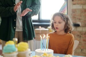 Child blowing out candles on a birthday cake, wearing a party hat.