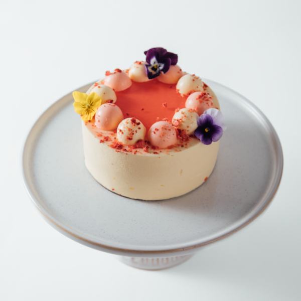 Orange Blossom 1 Elegant cake with pink frosting and edible flowers on a stand.
