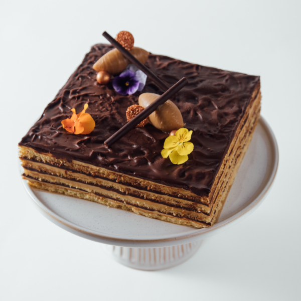 Hazelnut Opera 1 Layered chocolate cake with decorative flowers and chocolate sticks on a white cake stand.