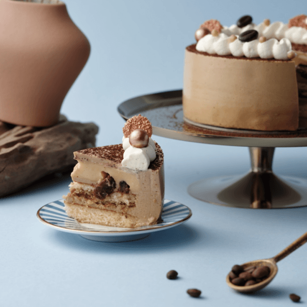 Coffee-flavored cake slice on plate, whole cake in background.