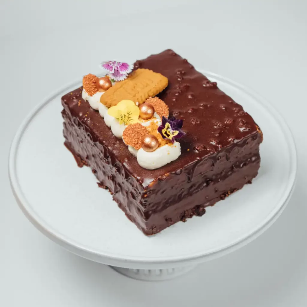 chocolate cake with cream, cookies, and flowers on a white stand