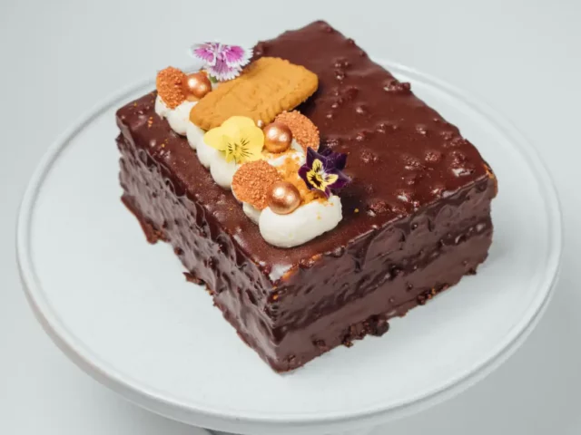 chocolate cake with cream, cookies, and flowers on a white stand